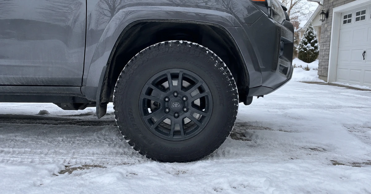 An All Terrain Tire for Snow sits mounted on a parked vehicle in a snowy driveway