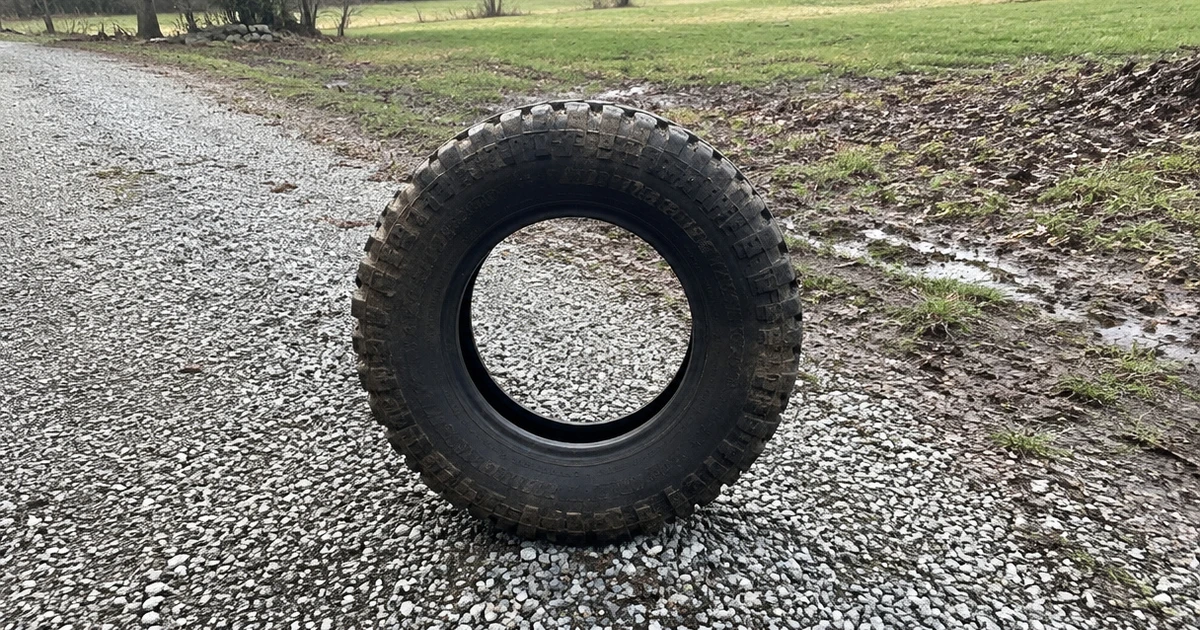 A Budget All Terrain Tire stands upright on a worn gravel driveway