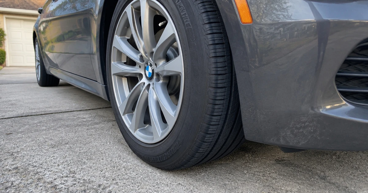 A Run Flat Tire fills the frame beside a parked car in a sunny driveway