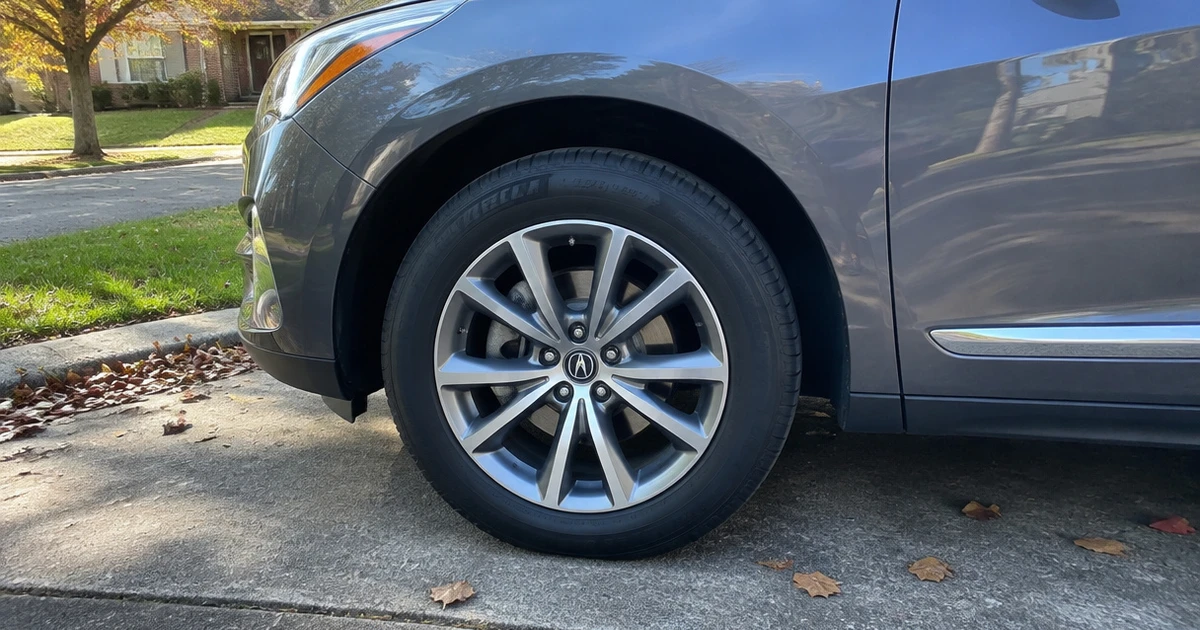 A tire for Acura RDX meets the pavement beside a sunlit driveway