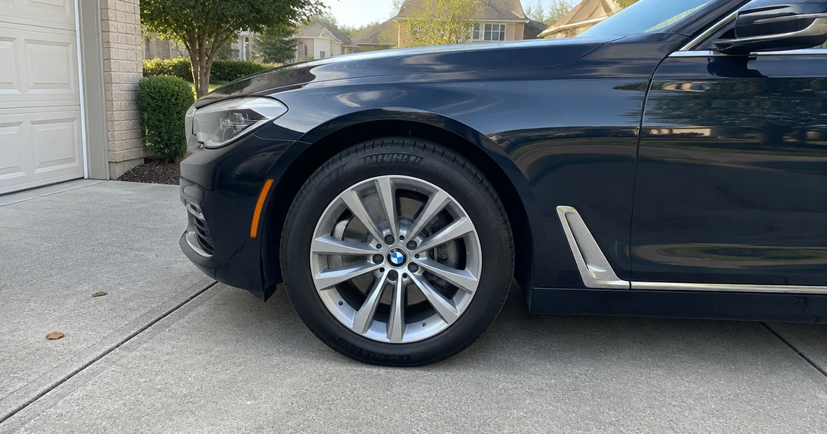 A tire for BMW 7 Series sits fitted on a parked sedan outdoors