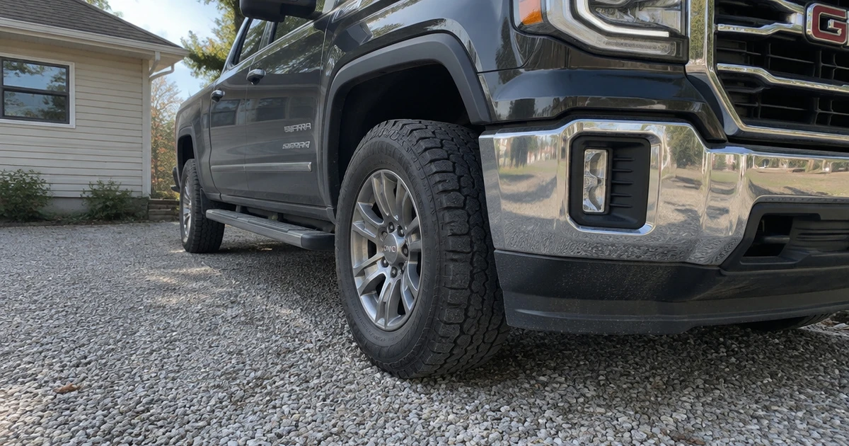 A tire for GMC Sierra grips a gravel driveway beneath a parked pickup
