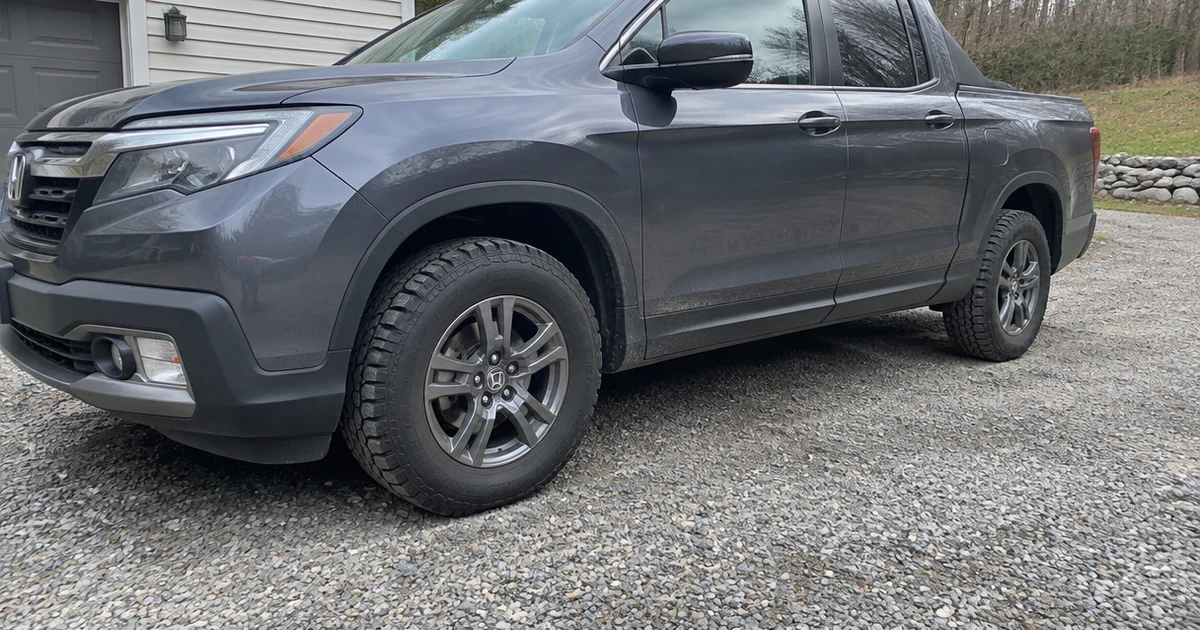 A Honda Ridgeline parked on a gravel drive with tires for Honda Ridgeline clearly visible