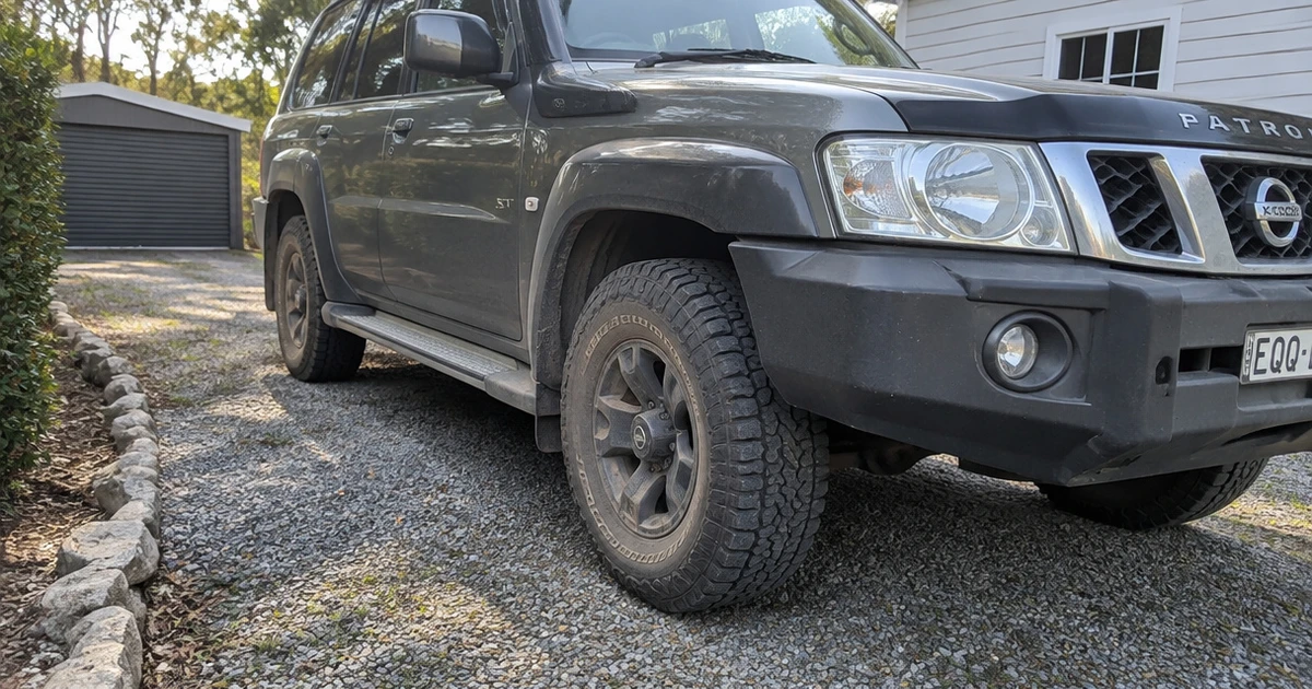 A Nissan Patrol sits on a gravel driveway with tires for Nissan Patrol mounted