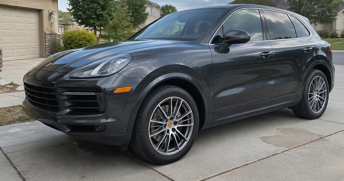 A tire for Porsche Cayenne meets the pavement beneath a parked SUV in a quiet driveway